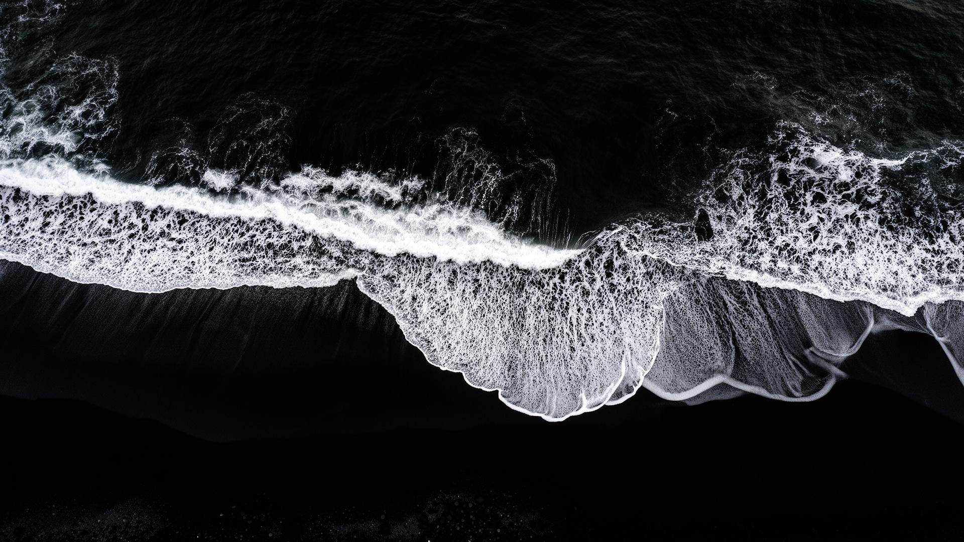Aerial view of dark ocean waves on black sand